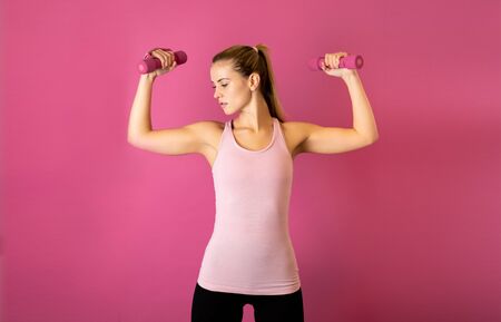 Attractive fitness woman holding dumbells on pink backgroundの写真素材