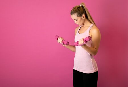 Attractive fitness woman holding dumbells on pink backgroundの写真素材