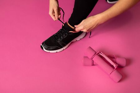 Woman tying sport shoes on pink backgroundの写真素材