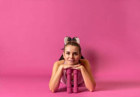 Athletic woman with dumbbells lying on pink background with copy spaceの写真素材