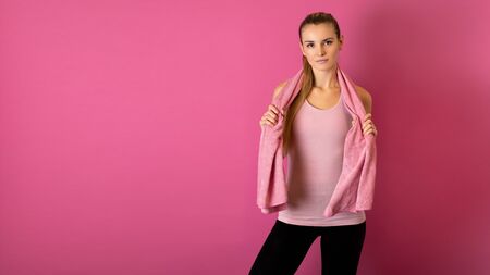 Fit woman after workout with towel on her shoulders on pink backgroundの写真素材