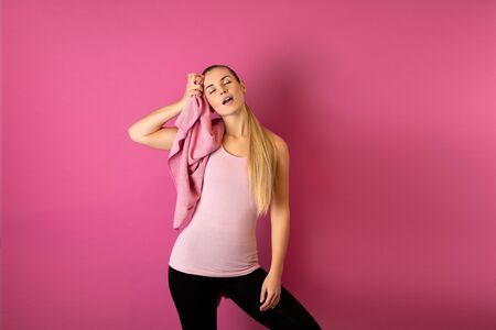 Young fit woman tired after workout with towel on her shoulders on pink backgroundの写真素材