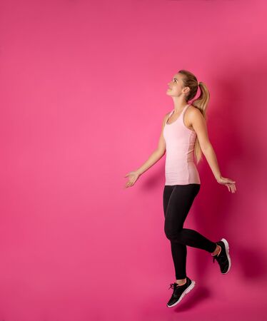Young fit woman jumping on pink background with copy spaceの写真素材