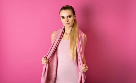 Fit woman after workout with towel on her shoulders on pink backgroundの写真素材