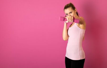 Attractive fitness woman holding dumbells on pink backgroundの写真素材