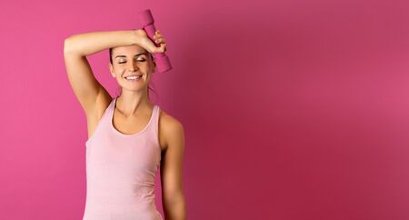 Young fit woman holding dumbell on pink backgroundの写真素材