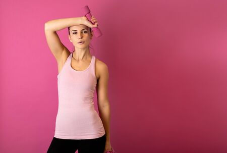 Young fit woman holding dumbell on pink backgroundの写真素材