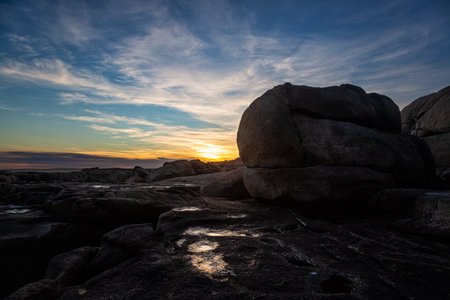 Sunset at the beach with rocks in the foreground and blue skyの写真素材