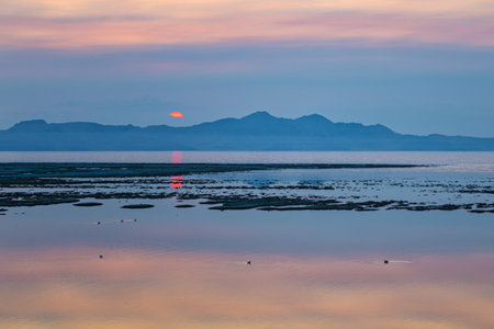 Sunset over the sea with reflection in the water and mountains in the backgroundの写真素材