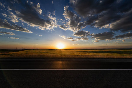 Asphalt road through the field at sunset with dramatic sky background.の写真素材