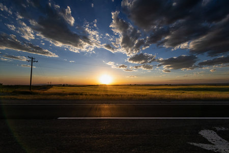 Sunset over the field with a road in the foreground and dramatic skyの写真素材