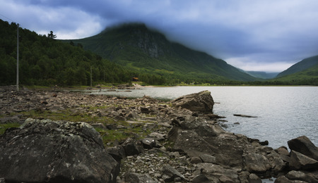 Rocky shore of a lake near a mountain in clouds in Norwayの写真素材
