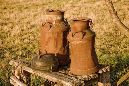 Two old milk jugs standing on a old benchの写真素材