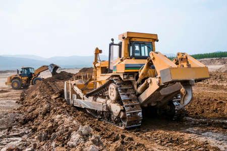 Bulldozer and front loader rake the ground Summer hot dusty day, construction machinery,の写真素材