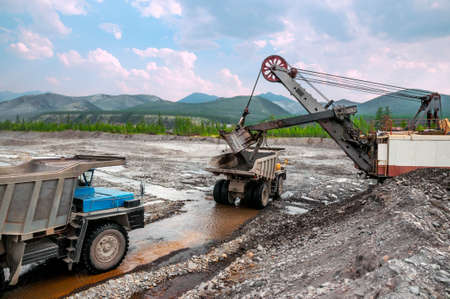 Gold mining industry. Loading with an excavator bucket and transportation of gold-bearing mountain...