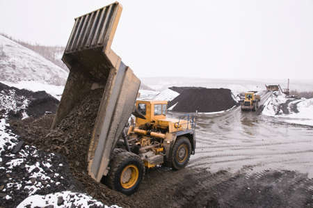 Excavation work in the highlands at the beginning of winter. A mining dump truck unloads mountain...