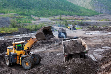 Front-end loader loads gold-bearing mountain soil into the back of a mining truck in a mountainous area.の写真素材