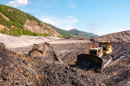 Bulldozer collects heap of mountain soil in which there is an increased concentration of natural gold Aurum Then wheel loaders transport this mountain soil to special industrial equipment for washingの写真素材