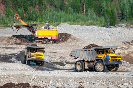 Loading of mountain soil into the body of a mining dump truck using an excavator, and further transportation of the cargo. Extraction of minerals in the mountainous region of Eastern Siberiaの写真素材