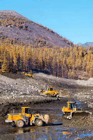 Bulldozer collects a heap of mountain soil in which there is increased concentration of natural gold...