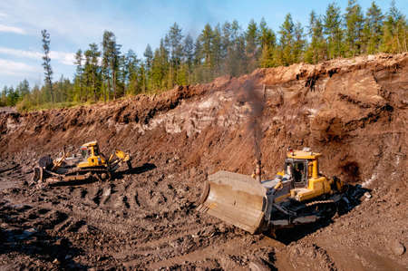 Excavation work in mountainous areas - mining. Bulldozers cut the top layer of the mountain soil and...
