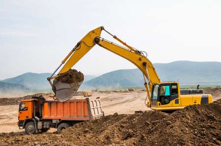 â¢ Earthworks, the excavator loads soil into the body of a cargo dump truckの写真素材