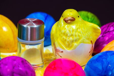 small salt shaker next to a clay chick and colorful Easter eggsの写真素材