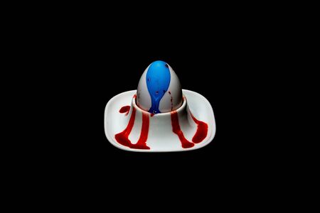 white fresh hen's egg in egg cup, blue and red colour runs down the egg
