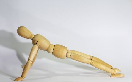 Wooden doll during yoga exercise Ansanas, the exercise inclined plane Purvotthasana, against white backgroundの写真素材