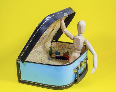 The lid of an old suitcase is held open by a wooden doll. Suitcase is packed for the next holidayの写真素材