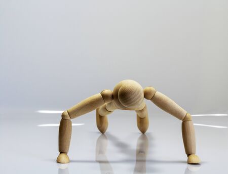 Wooden doll doing push-ups and reflections on the reflecting floorの写真素材