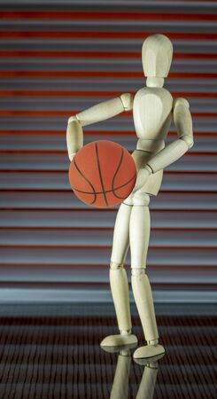 Wooden dummy with basketball in front of a jalousie plays with the ballの写真素材