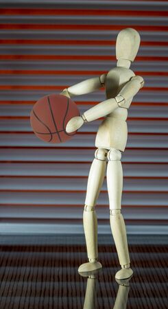 Wooden dummy with basketball in front of a jalousie plays with the ballの写真素材