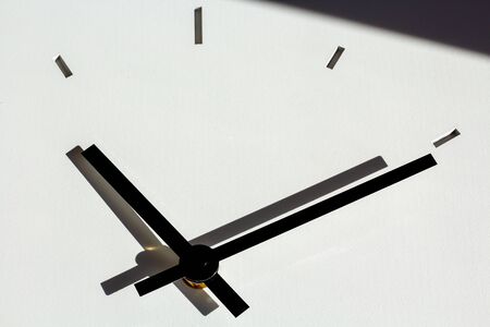 hands of a wall clock, with shadows on white, cementitious background structure. shadow in upper part of pictureの写真素材