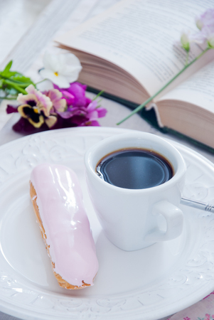 Breakfast - rose eclair and coffee cup with book and flowers