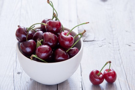 Cherries in a White Bowl on a light wooden backgroundの写真素材