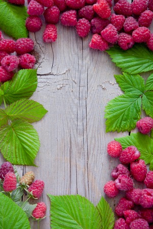Fresh organic raspberries with green leaves on a wooden background frameの写真素材