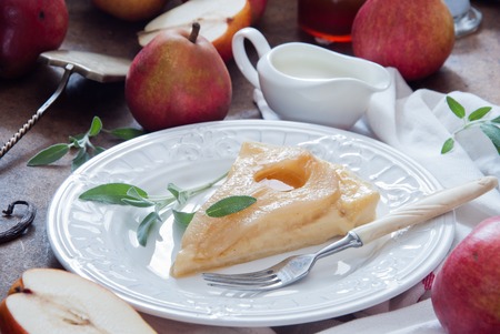 Piece of tart with roasted pears and vanilla custard with sage on a white plateの写真素材