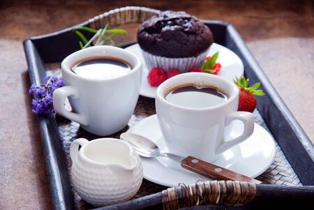 Black coffee in white cups and chocolate muffin with red berries on a dark wooden trayの写真素材