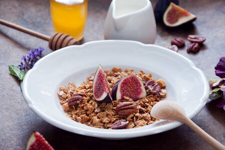 A healthy breakfast - homemade honey oatmeal granola with fresh figs in a white plate on a brown wooden backgroundの写真素材