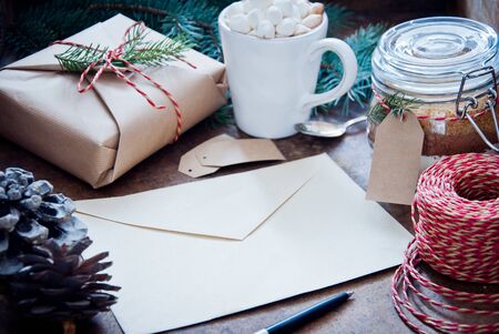 Christmas Envelope with a letter with Hot Chocolate with marshmallows and gifts decorated with pine cones and spruce branches on a dark wooden backgroundの写真素材