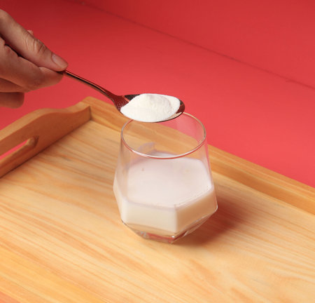 A person is holding a spoon with a glass of milk on itの写真素材