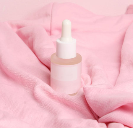 A bottle of liquid with a white cap sits on a pink blanket.の写真素材