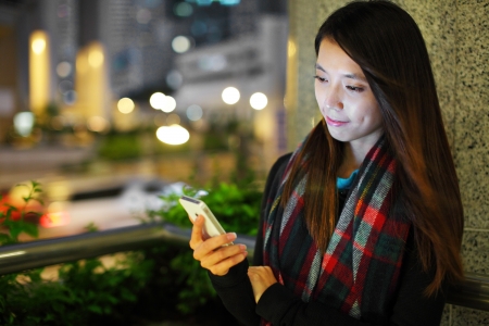 Woman using smartphone in city at nightの写真素材