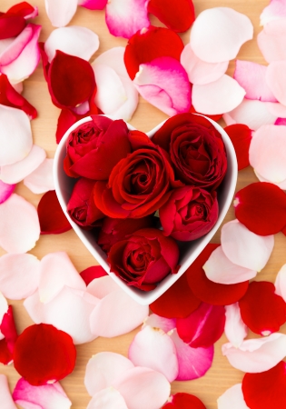 Red rose inside the heart shape bowl with pink petal besideの写真素材