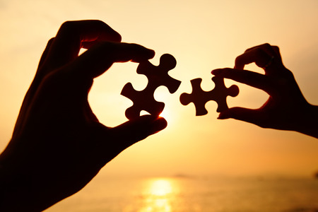Man and woman hands trying to connect puzzle pieces 