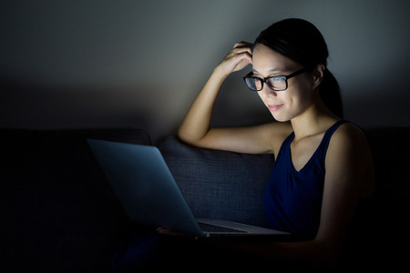 Woman lying with her laptop in night in the living roomの写真素材
