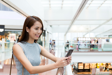 Asian woman reading something on mobile phone at shopping centerの写真素材