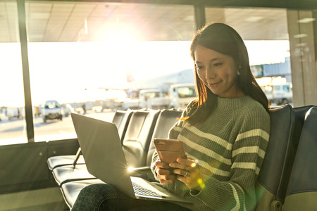 Woman look at cellphone with her laptop at airport