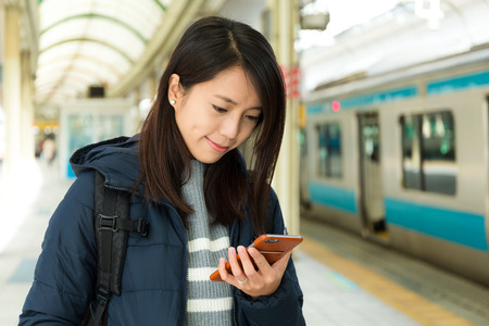 Woman reading message on cellphone in train stationの写真素材